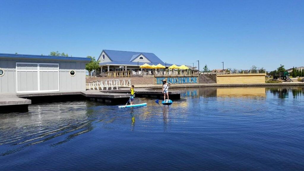 two people paddle boarding on a blue lake in front of a boathouse
