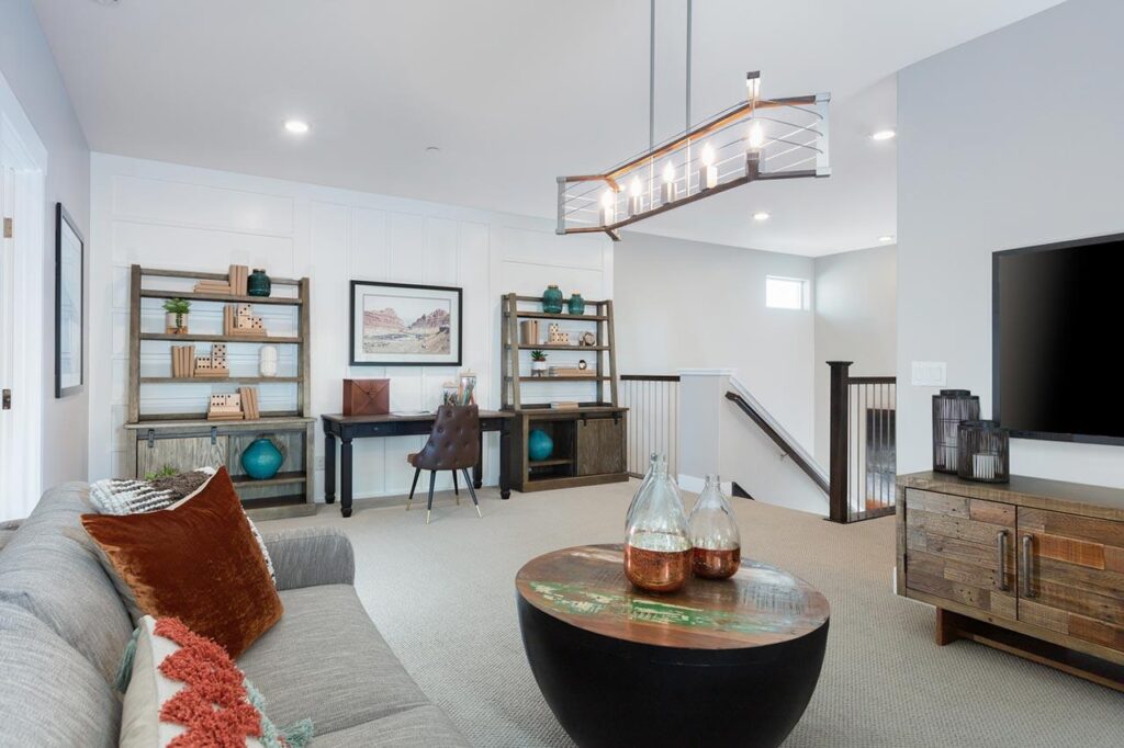 a modern living area with a couch, a television, a coffee table, a desk, two shelves, and hanging lights